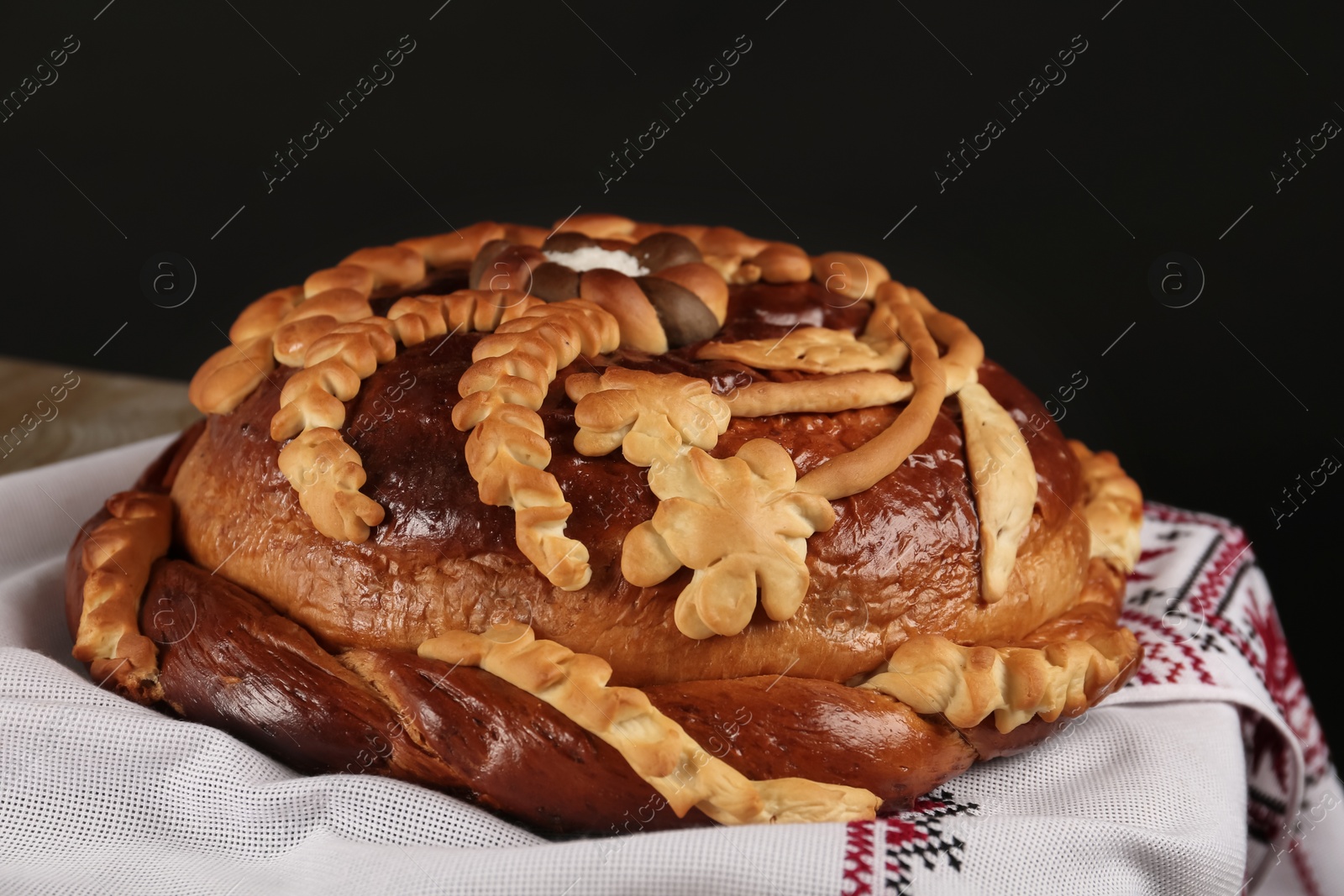 Photo of Rushnyk with korovai on table against black background, closeup. Ukrainian bread and salt welcoming tradition