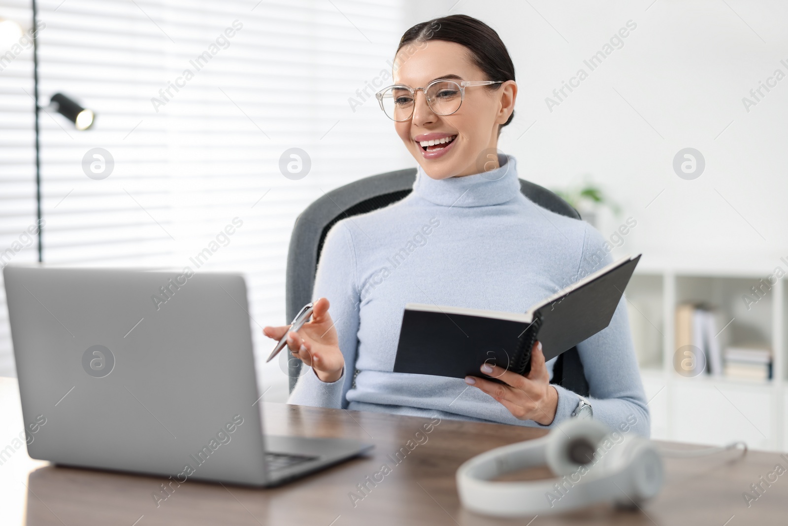 Photo of Young woman in glasses using video chat during webinar at table in office