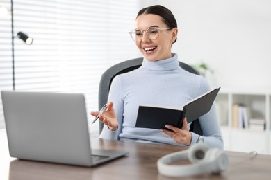 Photo of Young woman in glasses using video chat during webinar at table in office