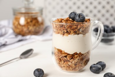 Photo of Tasty yogurt with muesli and blueberries in cup served on white wooden table