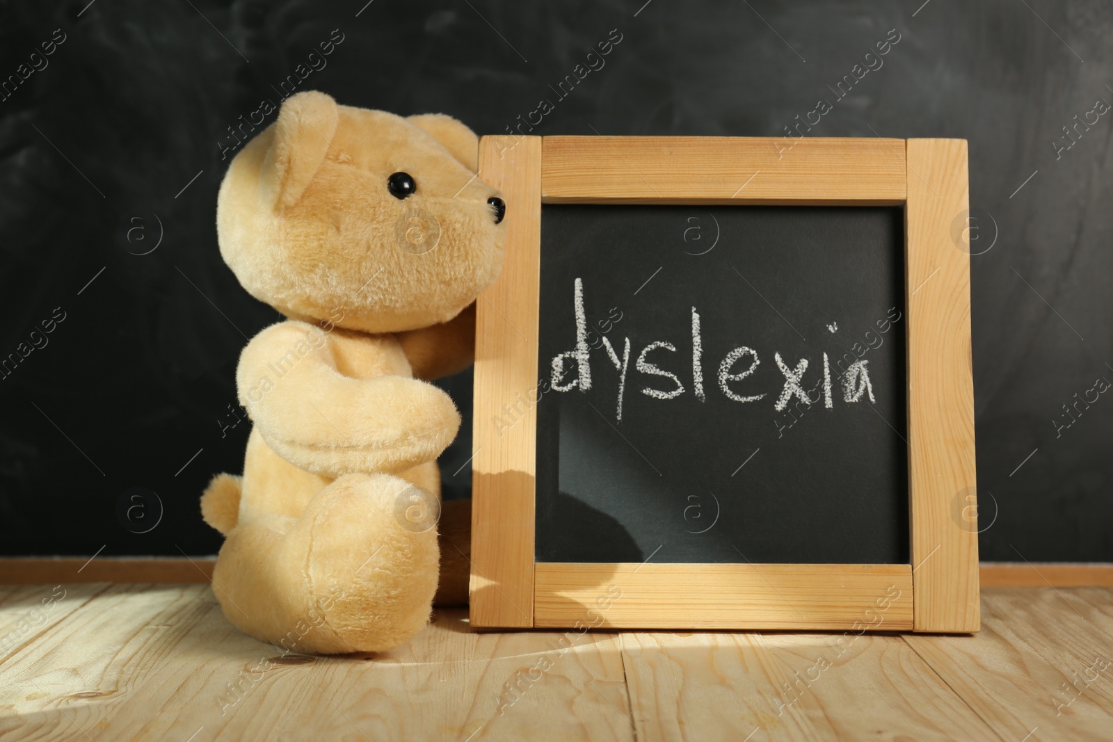 Photo of Teddy bear and small blackboard with word Dyslexia on wooden table