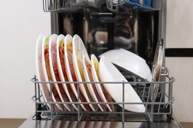 Photo of Open modern dishwasher with dirty tableware in kitchen