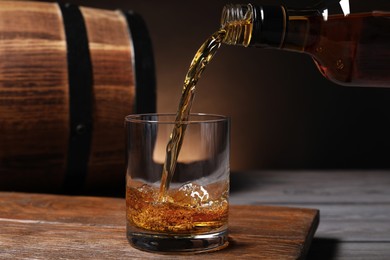 Photo of Pouring whiskey from bottle into glass on wooden table, closeup