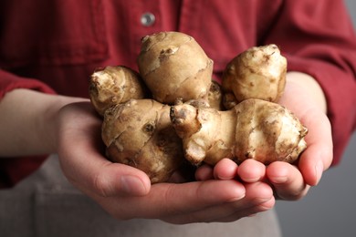 Photo of Woman holding Jerusalem artichokes on light grey background, closeup