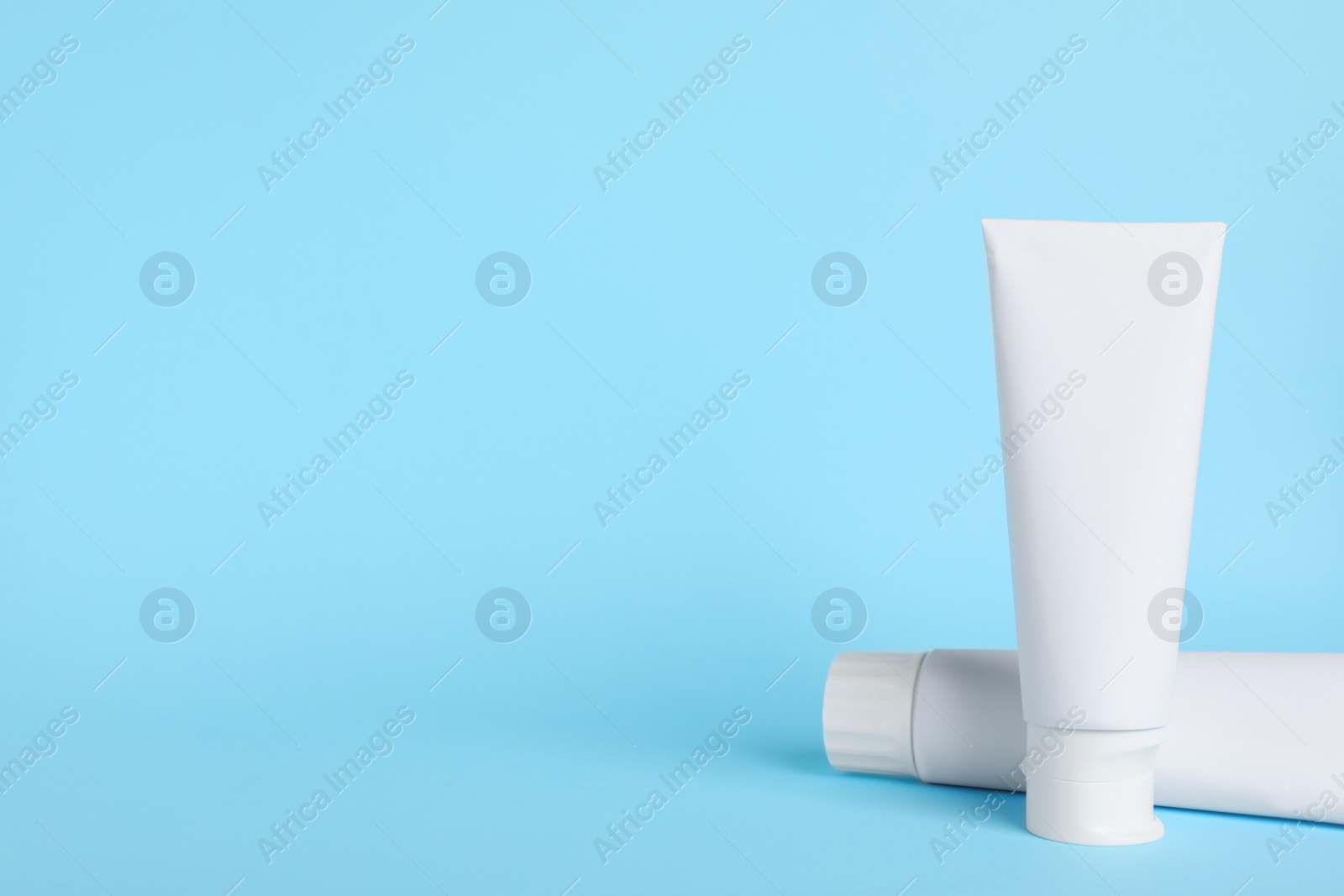 Photo of Blank tubes of toothpaste on light blue background. Space for text