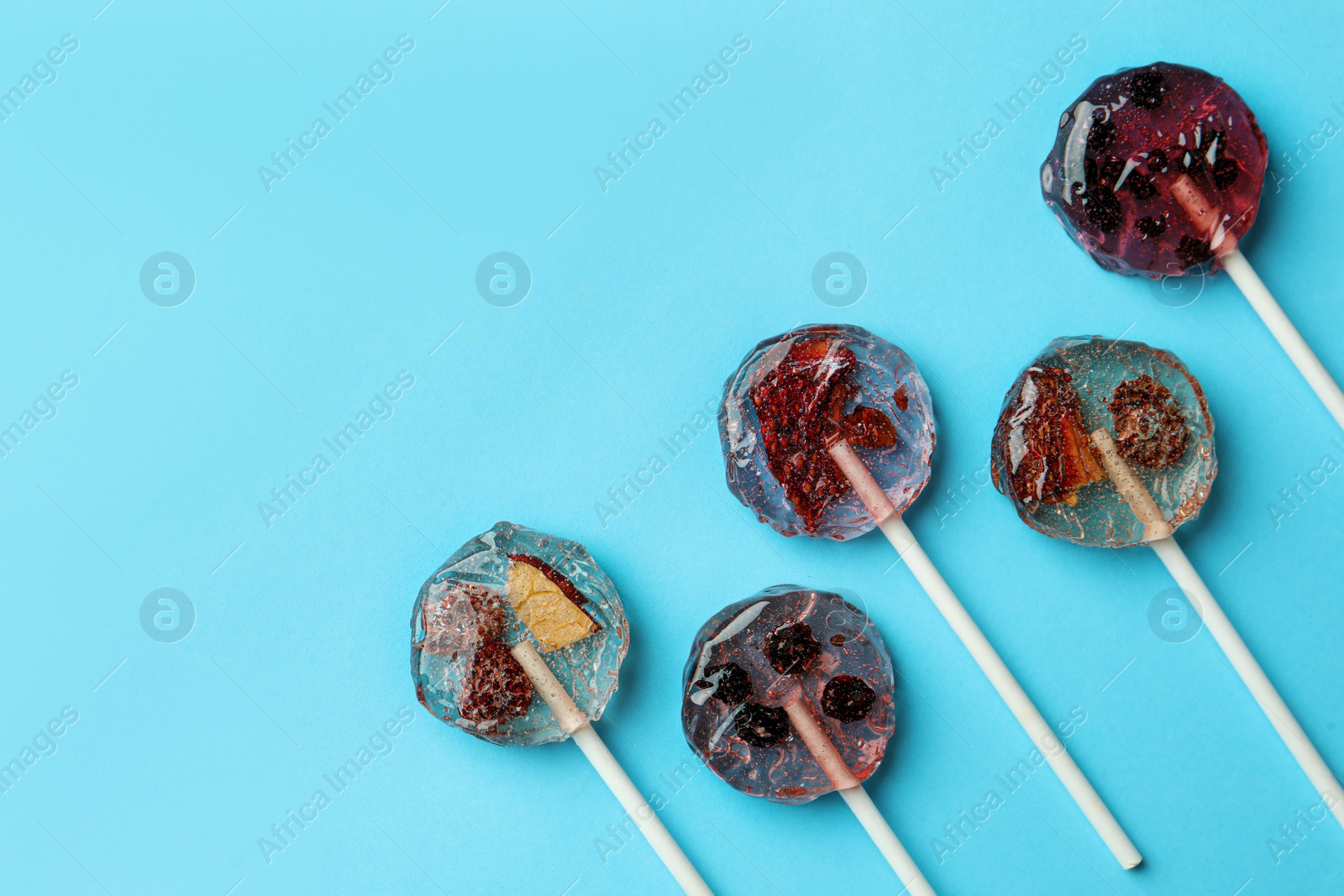 Photo of Sweet colorful lollipops with berries on light blue background, flat lay. Space for text