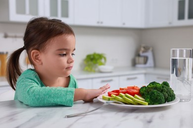 Cute little girl refusing to eat vegetables in kitchen