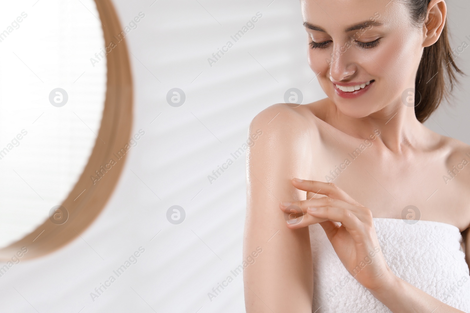 Photo of Happy woman applying body oil onto arm in bathroom, space for text