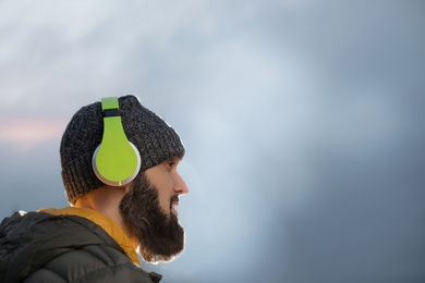 Photo of Mature man with headphones listening to music outdoors, space for text