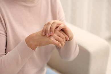 Mature woman suffering from pain in hand indoors, closeup. Rheumatism symptom