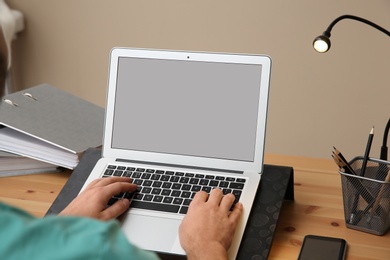 Photo of Young man using modern laptop at table, closeup