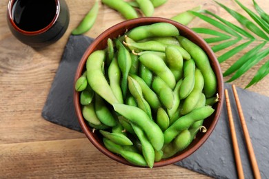 Photo of Green edamame beans in pods served with soy sauce on wooden table, flat lay