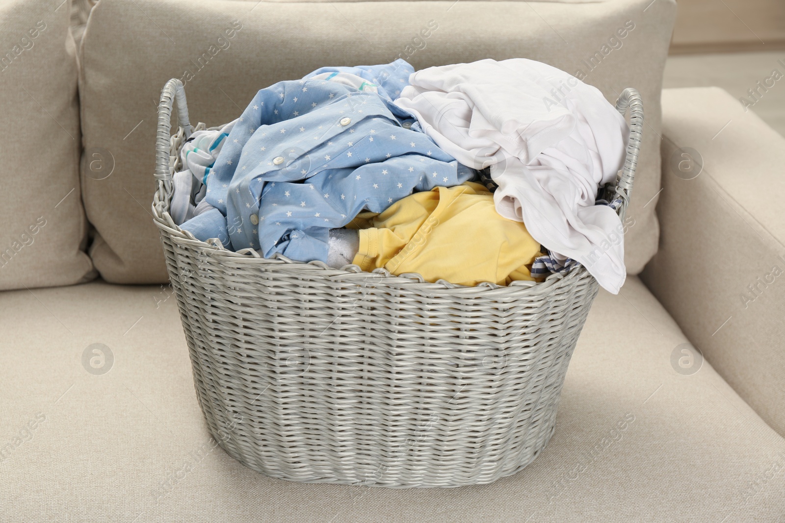 Photo of Wicker basket with dirty laundry on sofa in room