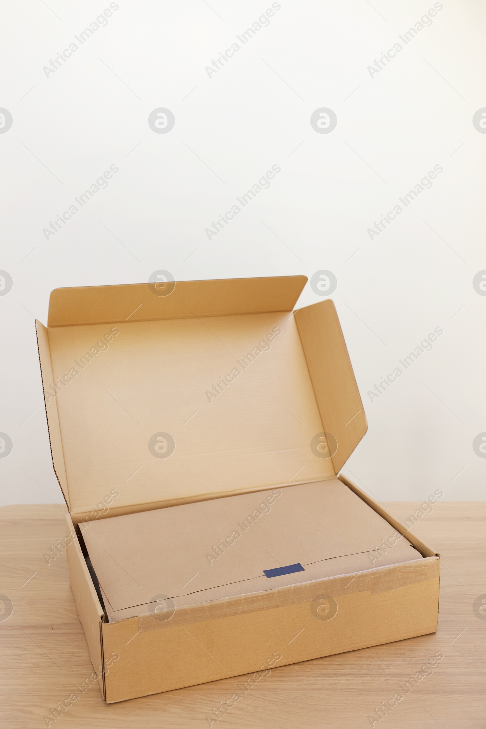 Photo of Open cardboard box with item wrapped in kraft paper on wooden table. Delivery service