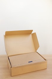 Photo of Open cardboard box with item wrapped in kraft paper on wooden table. Delivery service