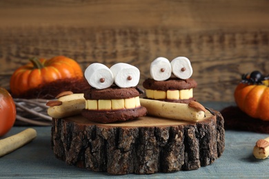 Photo of Delicious desserts decorated as monsters on blue wooden table. Halloween treat