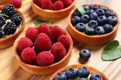 Photo of Tartlets with different fresh berries on wooden board, closeup. Delicious dessert