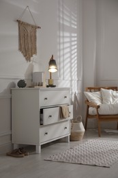 Stylish room interior with white chest of drawers and comfortable armchair