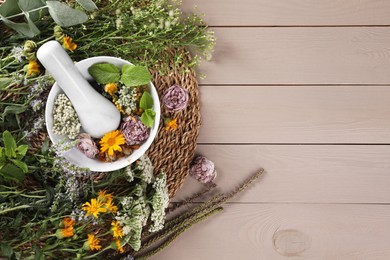 Photo of Mortar with pestle and many different herbs on wooden table, flat lay. Space for text