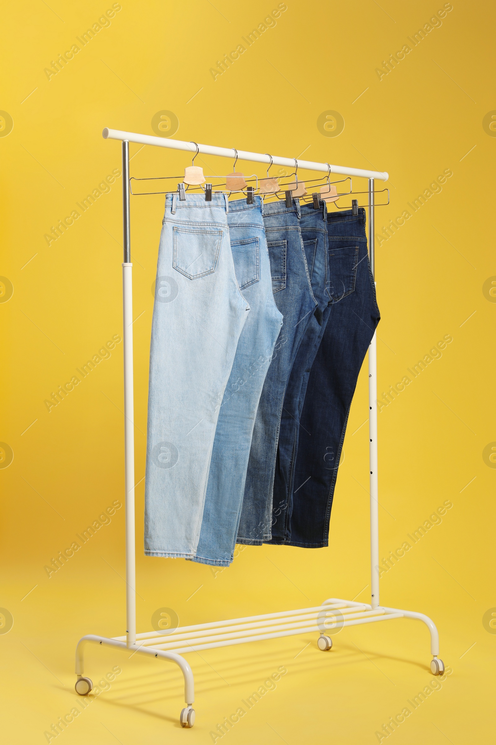 Photo of Rack with different jeans on yellow background