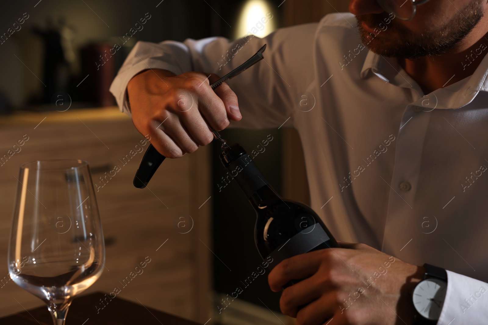 Photo of Romantic dinner. Man opening wine bottle with corkscrew indoors, closeup