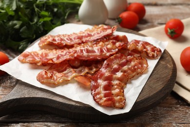 Photo of Fried bacon slices, tomato and parsley on wooden table, closeup