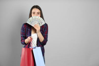 Young woman with money and shopping bags on light grey background. Space for text