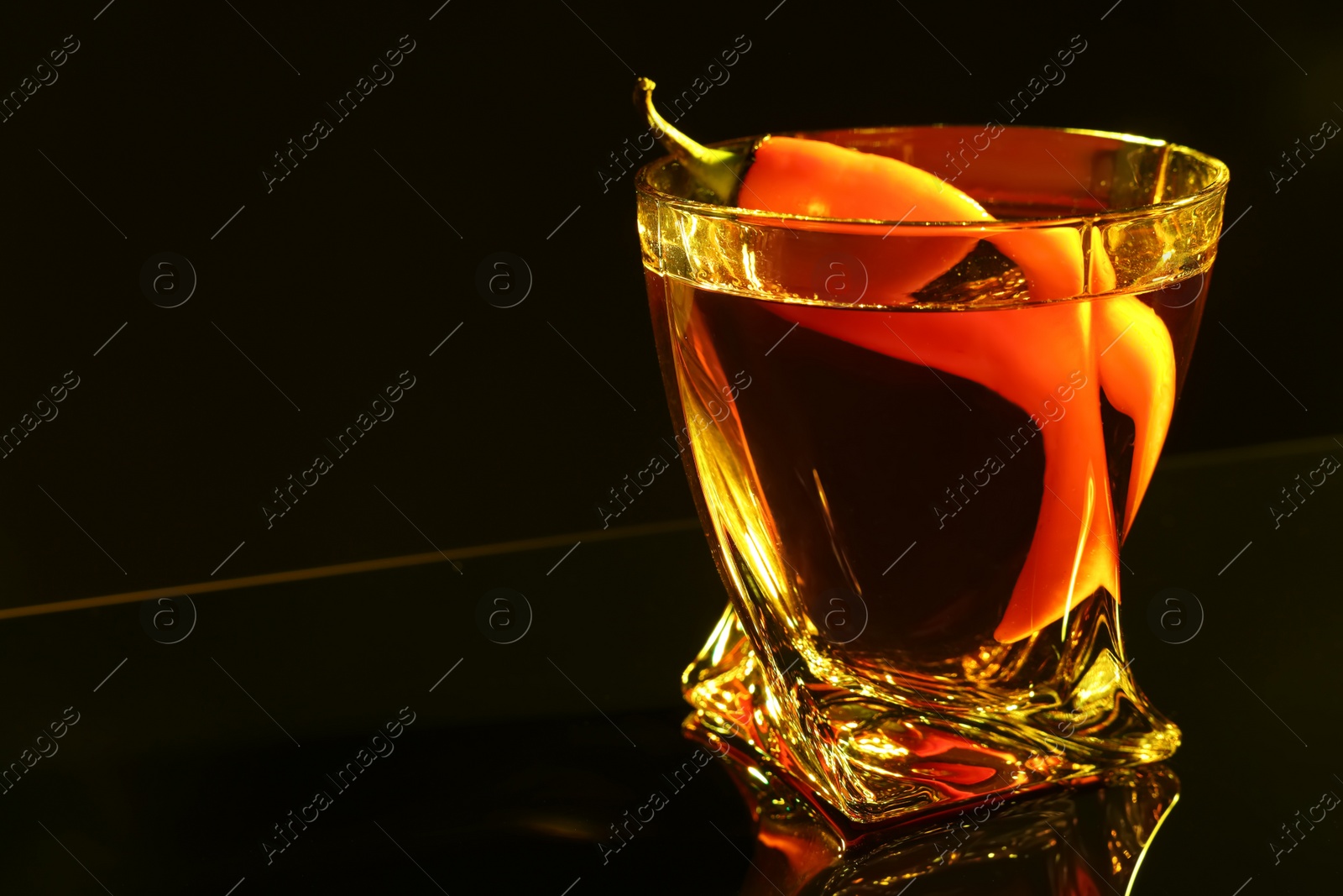 Photo of Red hot chili pepper and vodka on dark table, closeup. Space for text