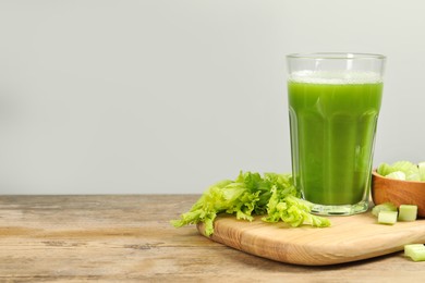 Glass of celery juice and fresh vegetables on wooden table, space for text