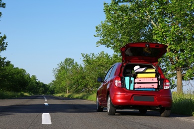 Photo of Family car with open trunk full of luggage on highway. Space for text