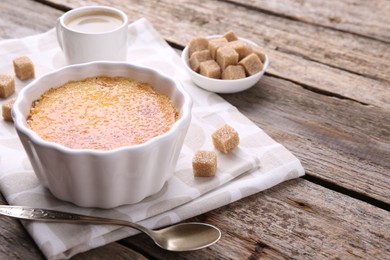 Delicious creme brulee in bowl, sugar cubes and spoon on wooden table, closeup