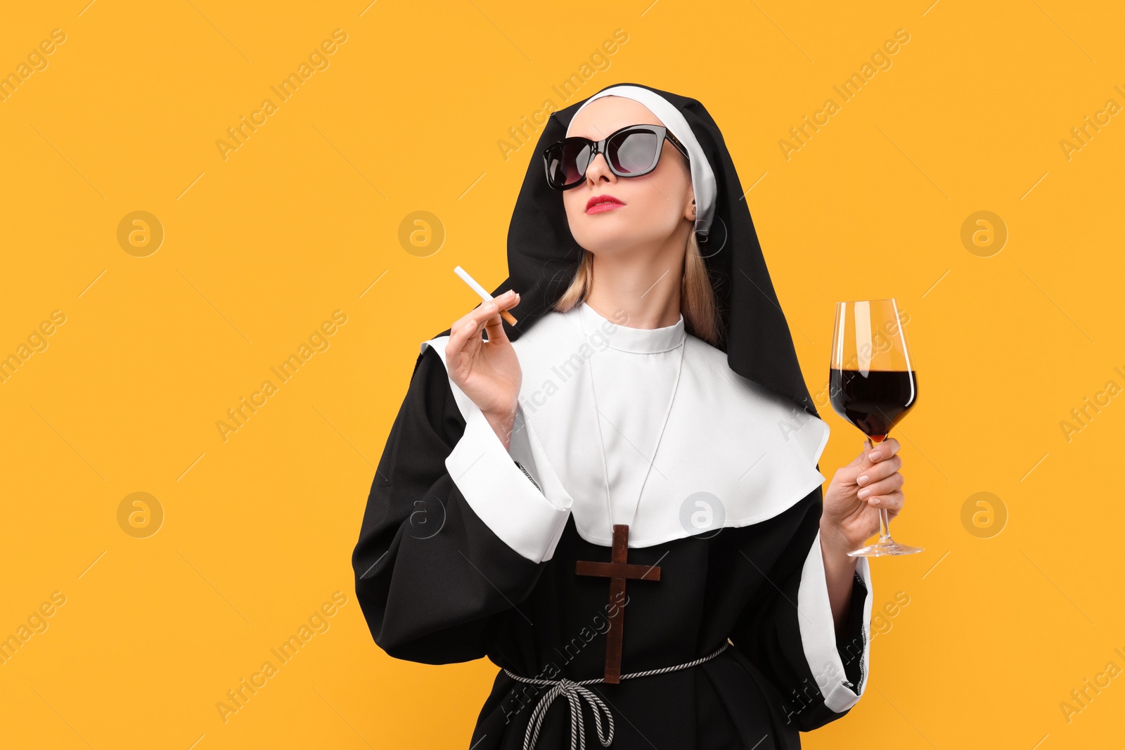 Photo of Woman in nun habit holding glass of wine and cigarette against orange background