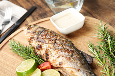 Photo of Delicious grilled fish with lime on wooden board, closeup