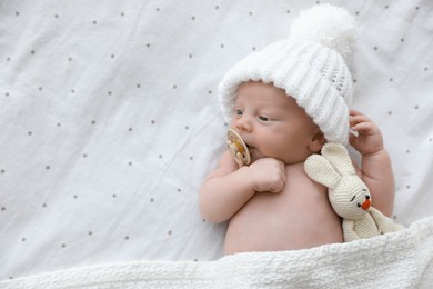 Photo of Cute newborn baby in white knitted hat with toy lying on bed, top view. Space for text