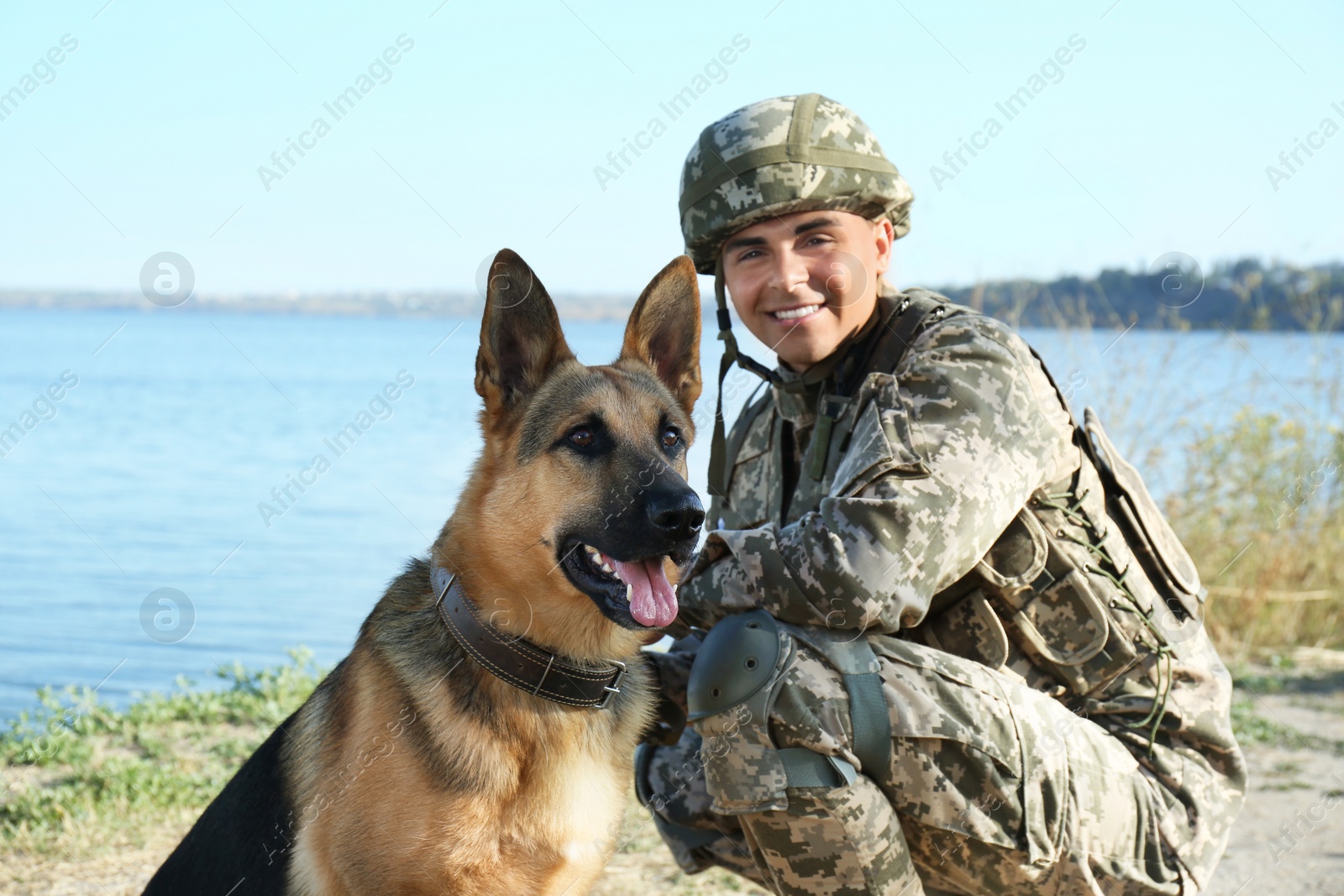 Photo of Man in military uniform with German shepherd dog near river