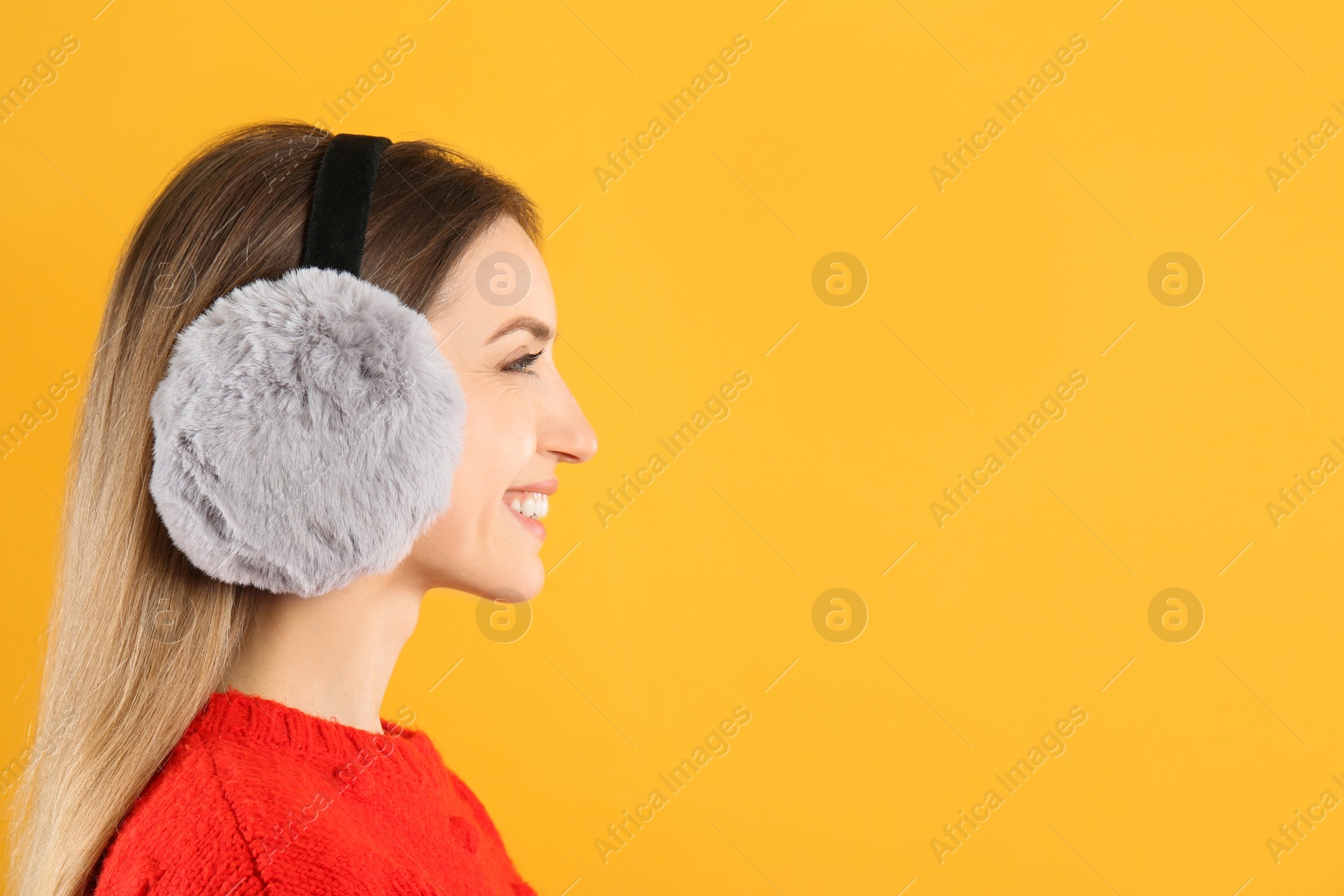 Photo of Happy woman wearing warm earmuffs on yellow background, space for text