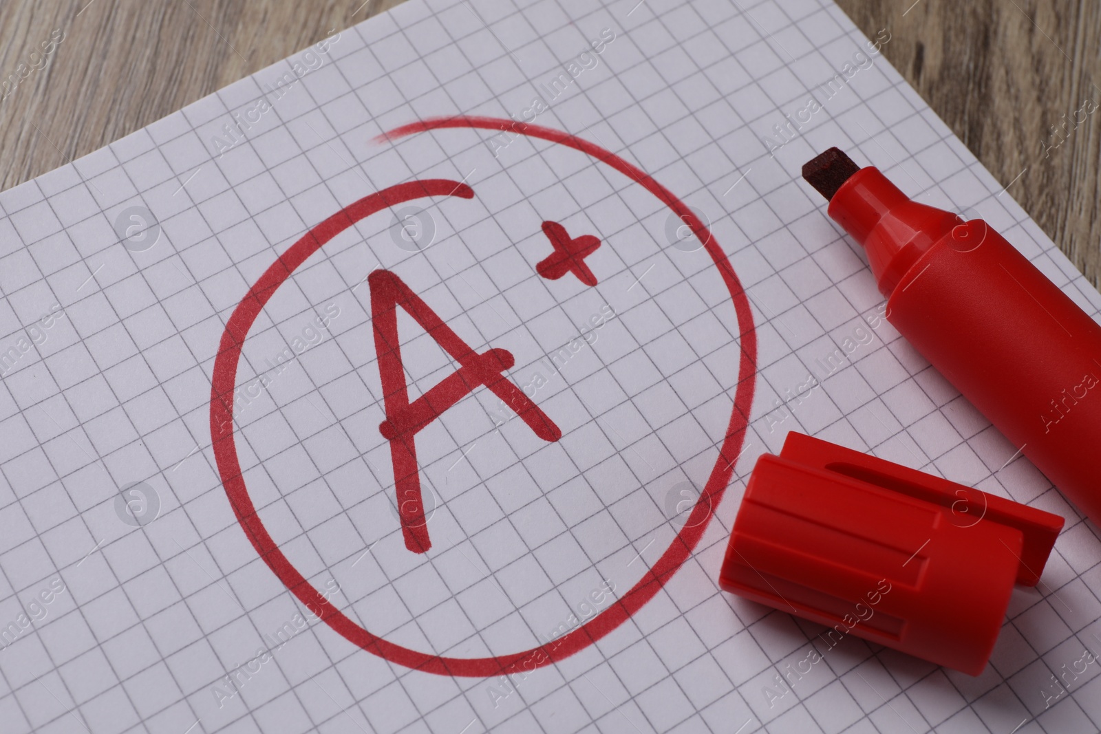 Photo of School grade. Red letter A with plus symbol on notebook paper and marker on table, closeup