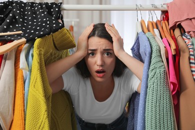 Photo of Upset young woman with lots of clothes on rack in room. Fast fashion