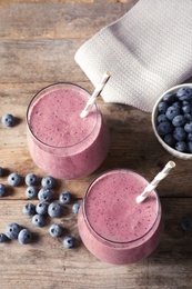 Photo of Tasty blueberry smoothie in glasses and berries on wooden table, above view