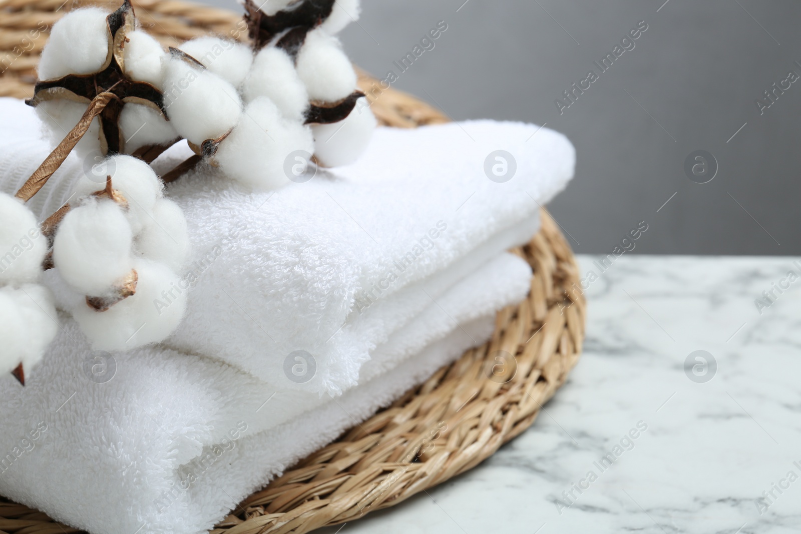 Photo of Folded terry towels and cotton flowers on white marble table, closeup