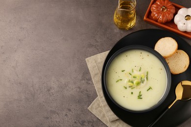 Photo of Bowl of tasty leek soup, spoon and bread on grey table, flat lay. Space for text