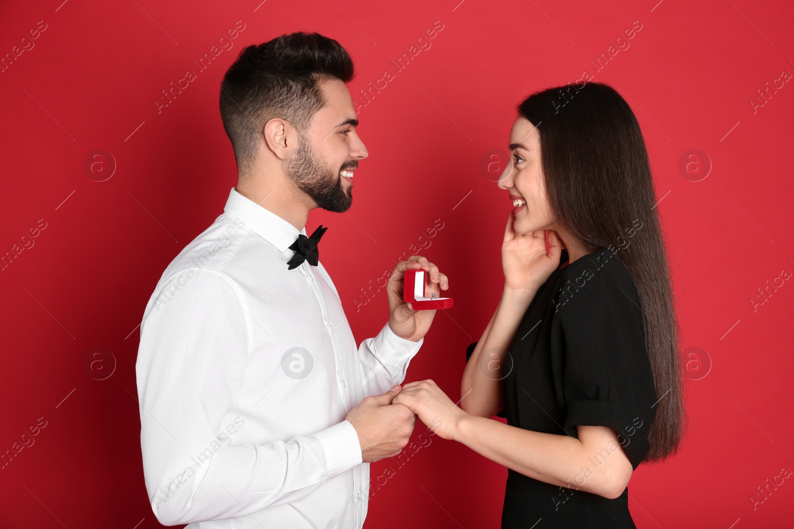 Photo of Man with engagement ring making marriage proposal to girlfriend on red background