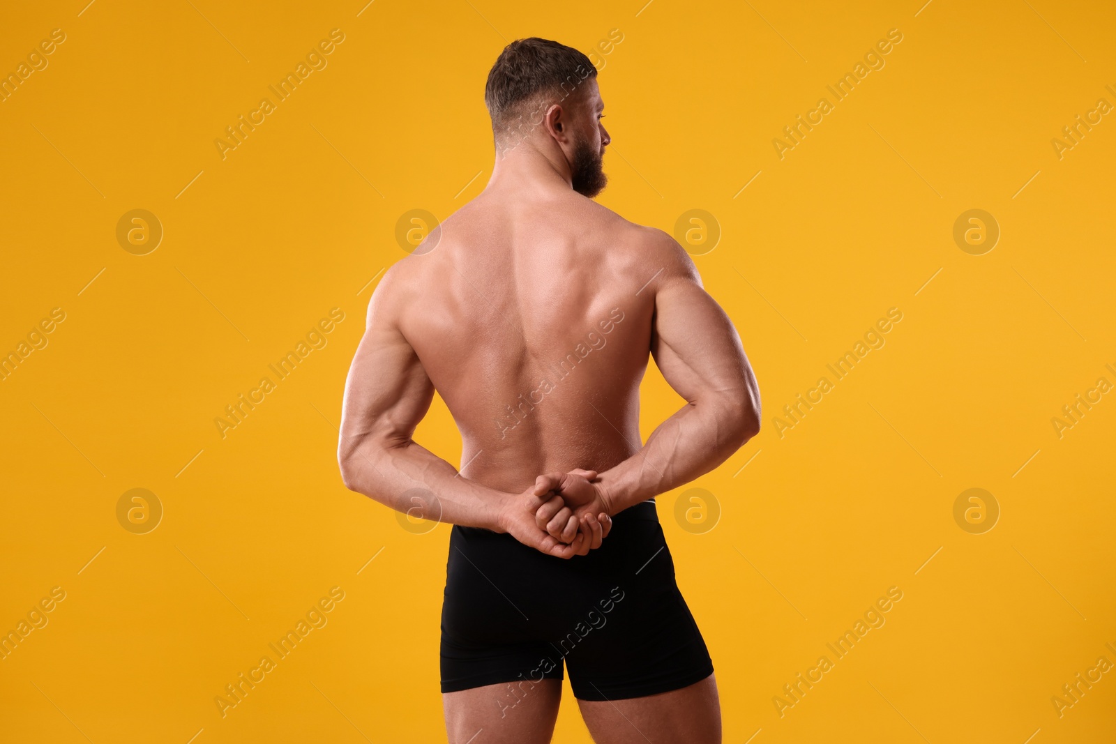 Photo of Young man is stylish black underwear on orange background, back view. Space for text