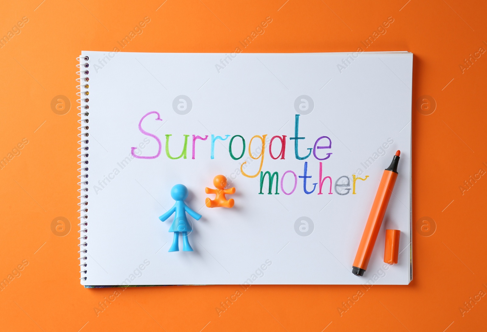 Photo of MYKOLAIV, UKRAINE - JANUARY 04, 2022: Notebook with words Surrogate Mother, marker and human figures on orange background, top view