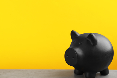 Black piggy bank on light grey table against yellow background. Space for text