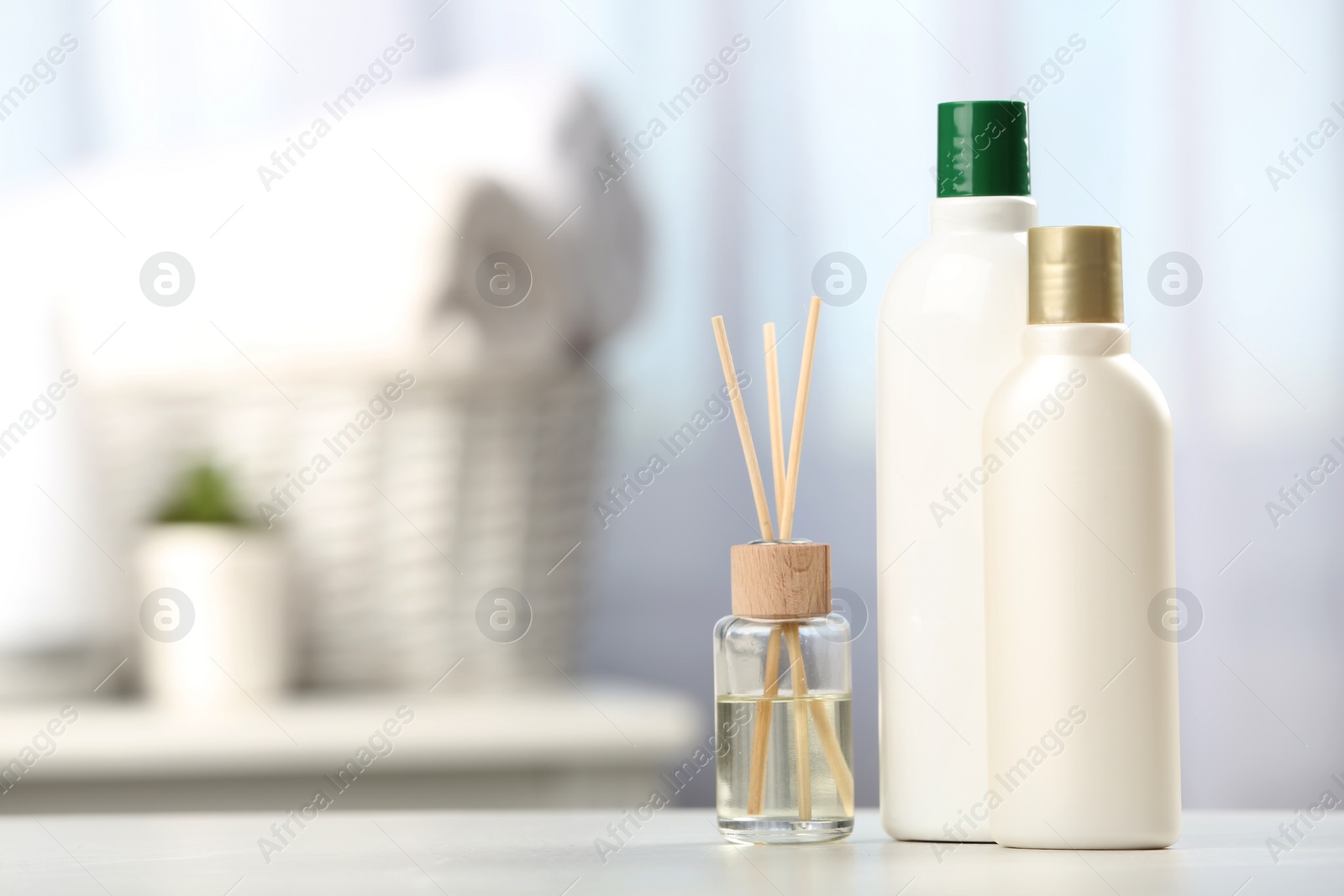 Photo of Bottles with hair care cosmetics and reed air freshener on table in bathroom, space for text