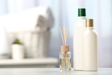 Bottles with hair care cosmetics and reed air freshener on table in bathroom, space for text