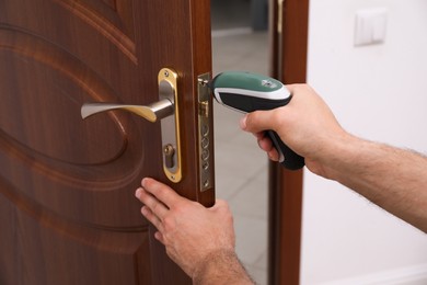 Photo of Handyman with screw gun repairing door lock indoors, closeup