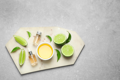 Lime essential oil and cut citrus fruits on light grey table, top view