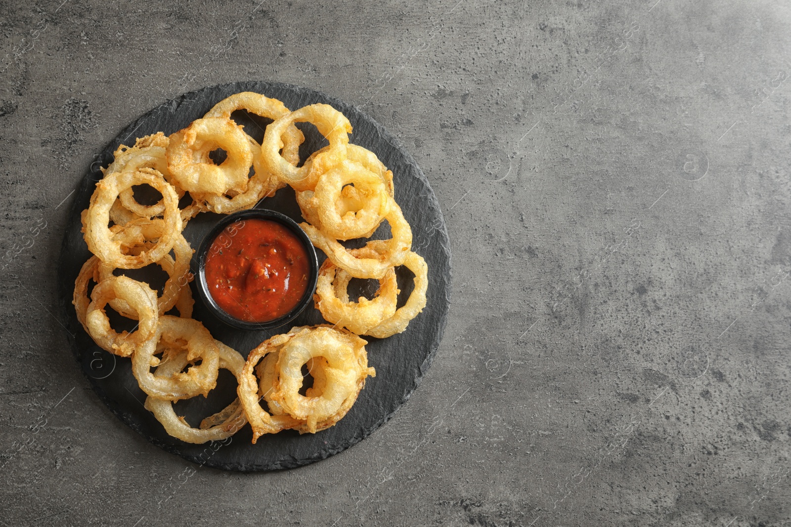 Photo of Delicious onion rings and sauce on gray background, top view. Space for text